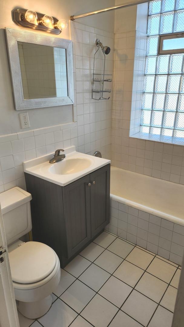 full bathroom featuring tile patterned flooring, toilet, vanity, tile walls, and tiled shower / bath