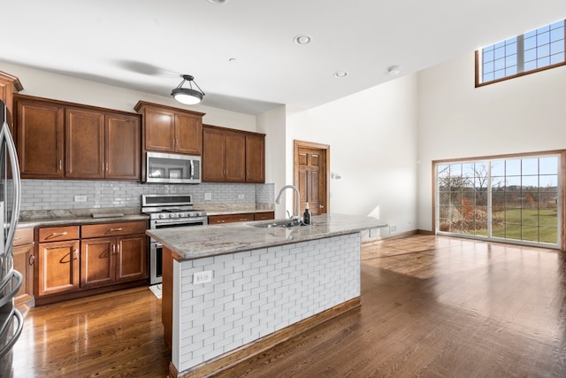 kitchen with dark wood-type flooring, a center island with sink, sink, light stone countertops, and stainless steel appliances