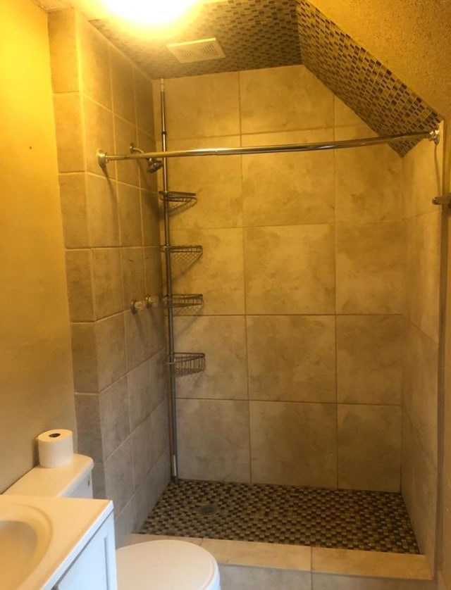 bathroom with a tile shower, vanity, and toilet