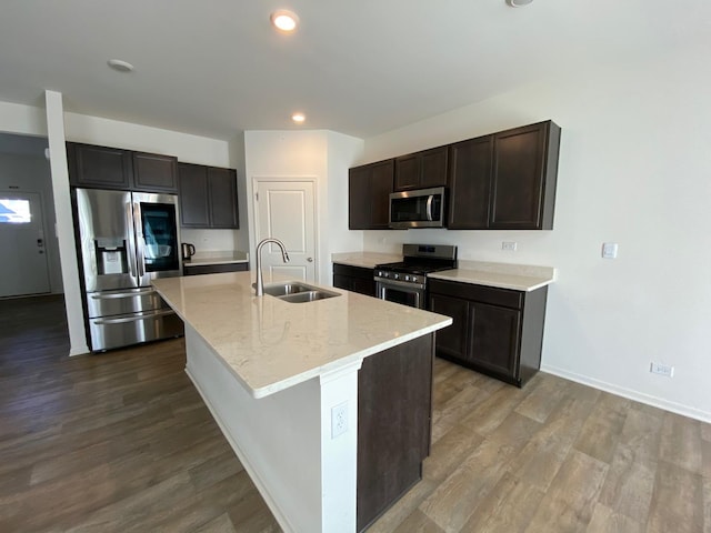 kitchen with dark brown cabinetry, stainless steel appliances, a kitchen island with sink, sink, and hardwood / wood-style floors