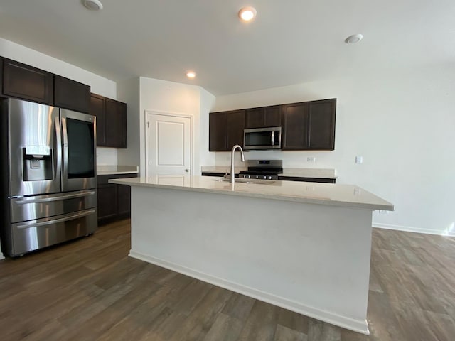 kitchen with dark wood-type flooring, a center island with sink, sink, appliances with stainless steel finishes, and dark brown cabinets