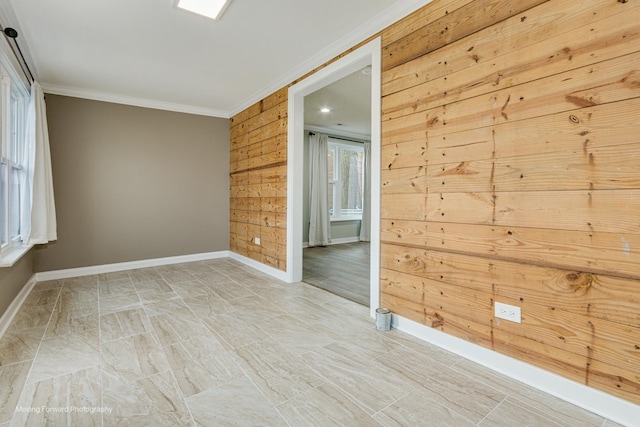 empty room featuring wood walls, ornamental molding, and a healthy amount of sunlight