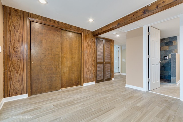 unfurnished bedroom featuring beam ceiling, light hardwood / wood-style floors, a closet, and wood walls