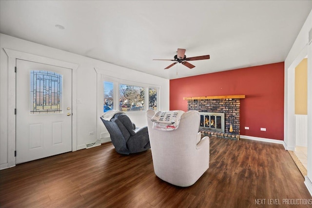 living room with a brick fireplace, ceiling fan, and dark wood-type flooring