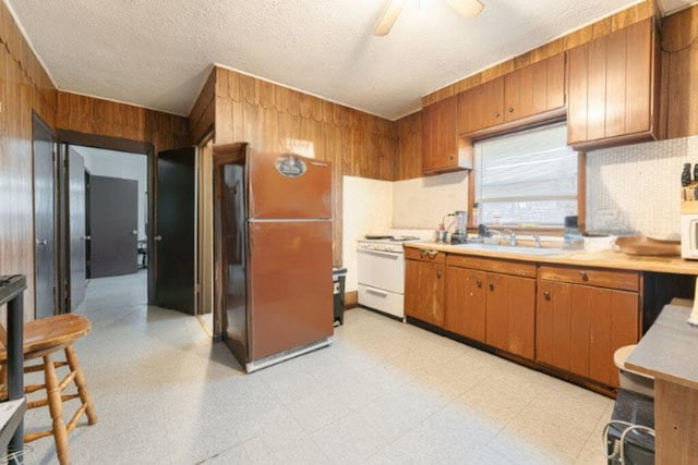 kitchen featuring sink, a textured ceiling, white appliances, and wood walls