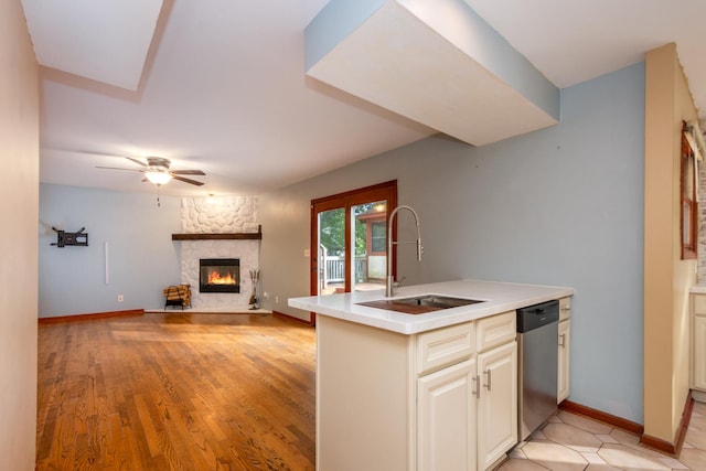 kitchen featuring sink, a stone fireplace, stainless steel dishwasher, and kitchen peninsula