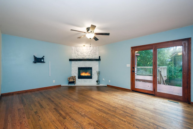 unfurnished living room featuring hardwood / wood-style floors, a stone fireplace, and ceiling fan