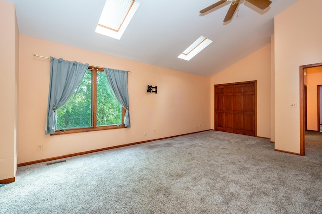 carpeted spare room with ceiling fan, high vaulted ceiling, and a skylight