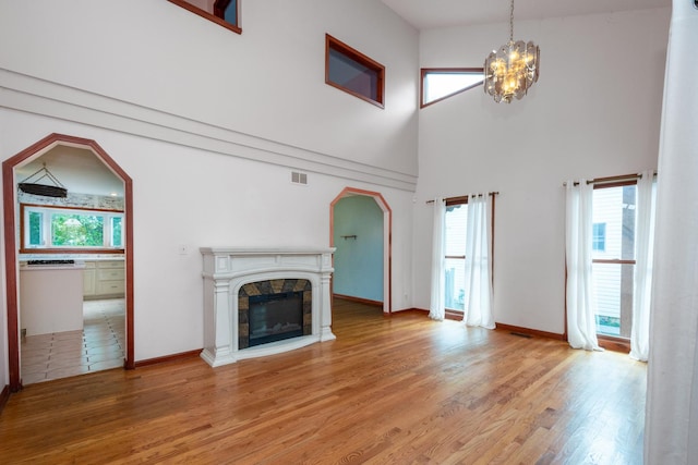 unfurnished living room featuring a towering ceiling, a stone fireplace, hardwood / wood-style floors, and a notable chandelier