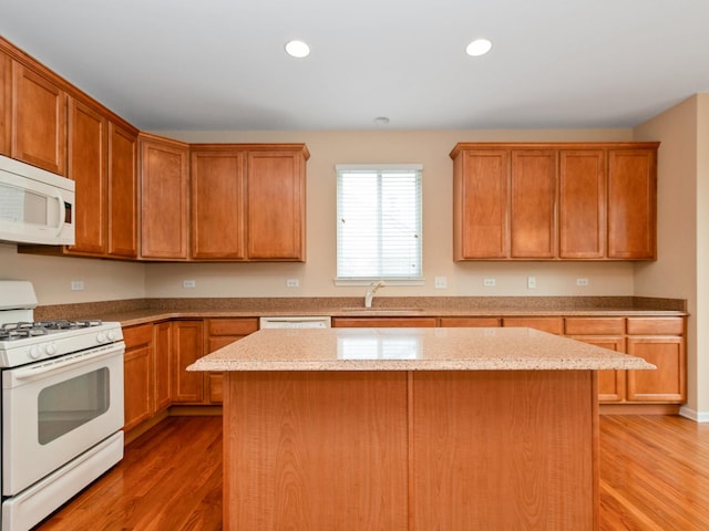 kitchen featuring wood-type flooring, sink, a center island, light stone countertops, and white appliances