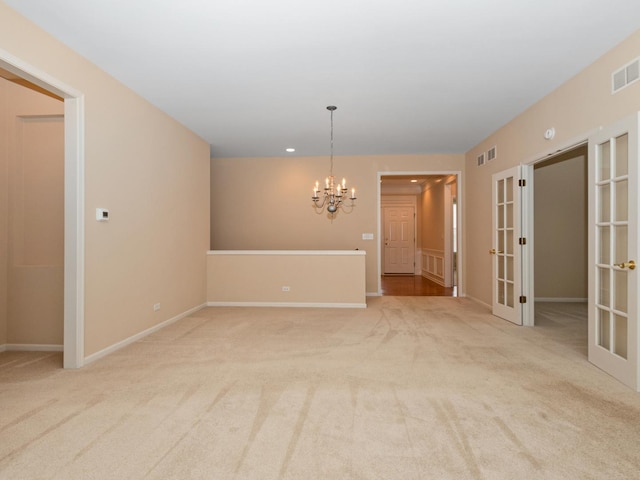 carpeted spare room with a notable chandelier and french doors