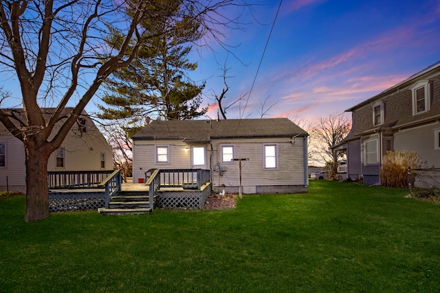 back house at dusk featuring a lawn and a deck