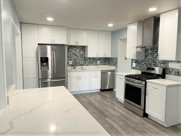 kitchen with light stone countertops, white cabinets, wall chimney range hood, and appliances with stainless steel finishes