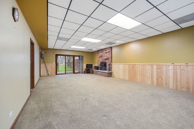 unfurnished living room featuring a brick fireplace, carpet, wood walls, and wainscoting