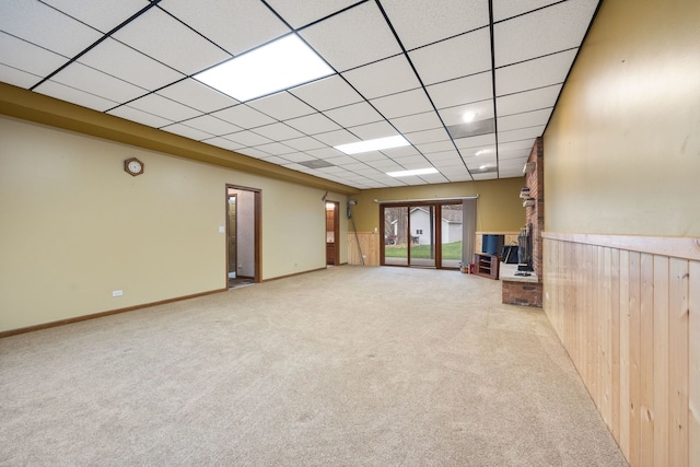 interior space featuring carpet floors, wood walls, a drop ceiling, and a wainscoted wall