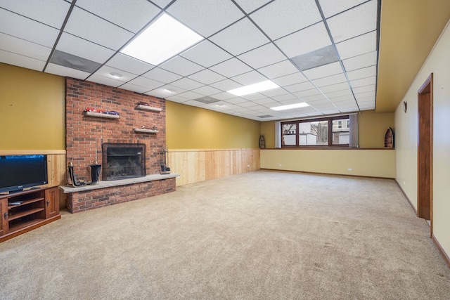 unfurnished living room with a wainscoted wall, a fireplace, carpet flooring, wooden walls, and a drop ceiling