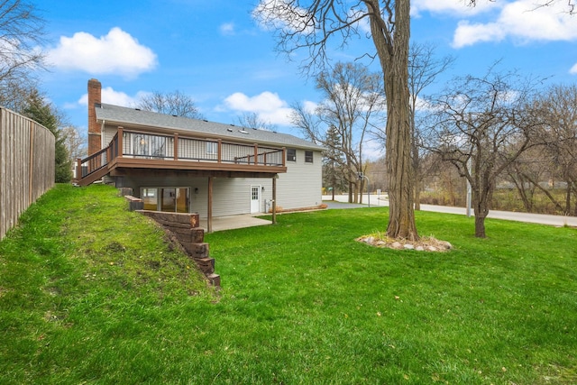 rear view of property featuring a chimney, a yard, a deck, and a patio