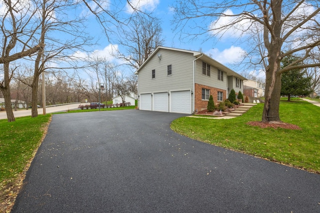 view of side of property with a garage, driveway, brick siding, and a lawn