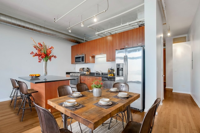 kitchen featuring a kitchen breakfast bar, track lighting, stainless steel appliances, sink, and light hardwood / wood-style flooring