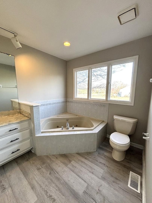 bathroom with tiled bath, vanity, wood-type flooring, and toilet