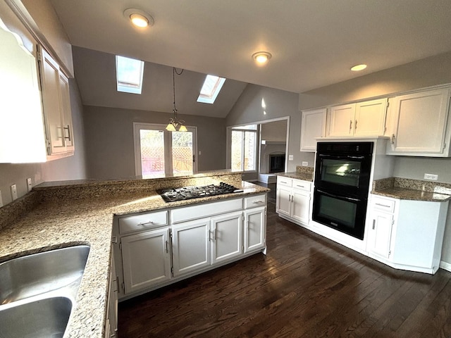 kitchen with white cabinets, black appliances, vaulted ceiling with skylight, decorative light fixtures, and dark hardwood / wood-style flooring