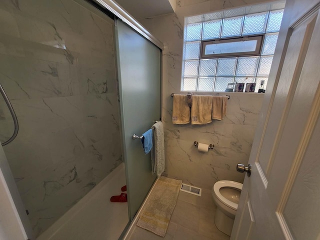 bathroom featuring tile patterned flooring, toilet, tile walls, and a shower with shower door