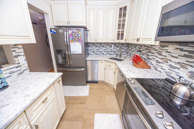 kitchen featuring decorative backsplash, light stone counters, sink, and appliances with stainless steel finishes