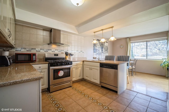 kitchen featuring backsplash, wall chimney range hood, hanging light fixtures, appliances with stainless steel finishes, and kitchen peninsula