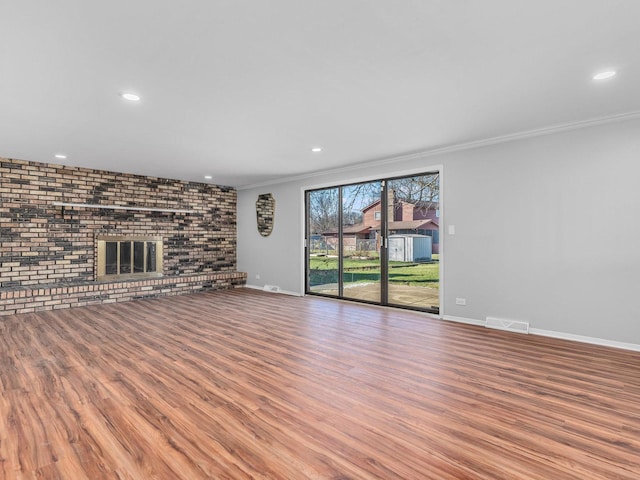 unfurnished living room featuring a fireplace, wood-type flooring, ornamental molding, and brick wall