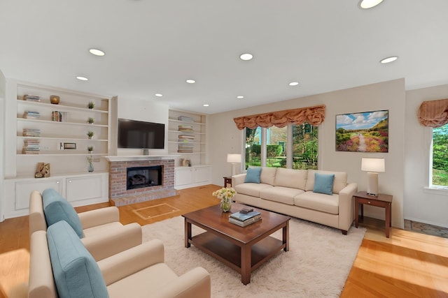 living room featuring built in shelves, a brick fireplace, and light hardwood / wood-style flooring