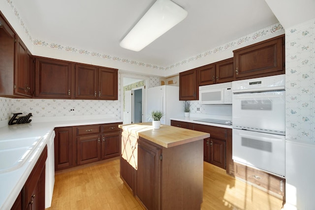 kitchen with white appliances, a kitchen island, sink, light wood-type flooring, and butcher block countertops