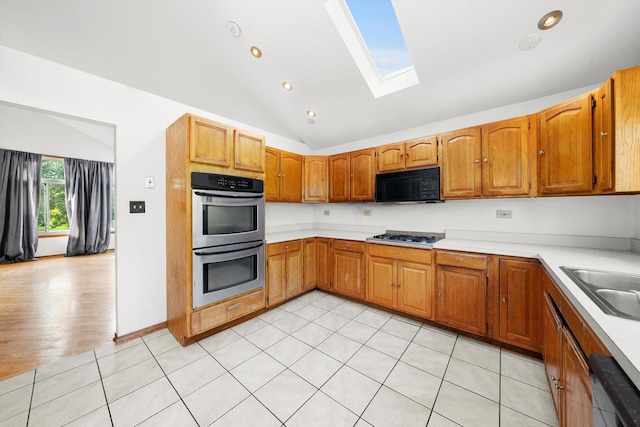 kitchen with lofted ceiling with skylight, sink, appliances with stainless steel finishes, and light hardwood / wood-style flooring