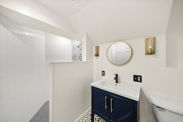 bathroom featuring a tile shower, vanity, toilet, and lofted ceiling