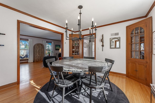 dining room featuring crown molding, light hardwood / wood-style floors, and a notable chandelier