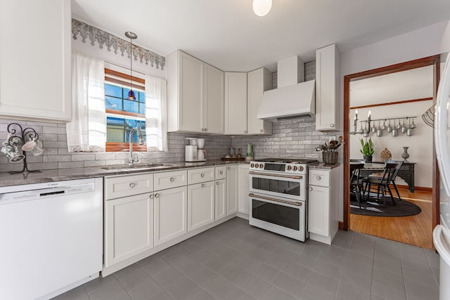 kitchen with wall chimney range hood, sink, white cabinetry, white dishwasher, and range with two ovens