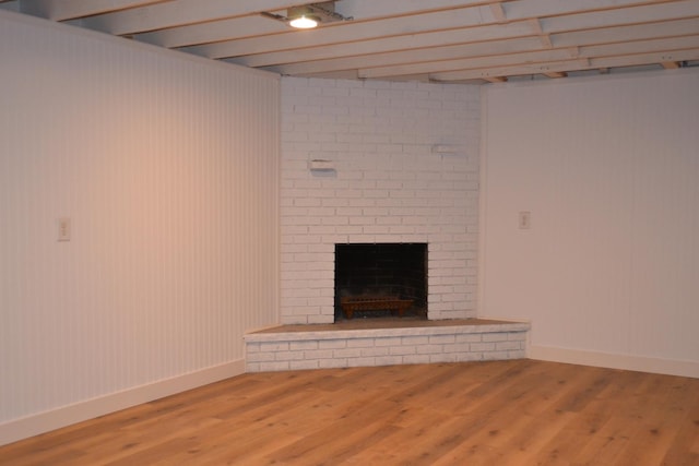 unfurnished living room with beam ceiling, hardwood / wood-style floors, and a brick fireplace