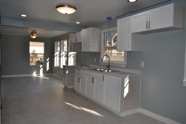 kitchen with hanging light fixtures, white cabinetry, ceiling fan, and sink