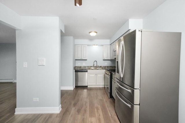 kitchen with white cabinets, appliances with stainless steel finishes, baseboard heating, and wood-type flooring