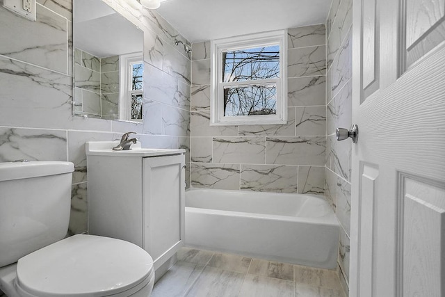 full bathroom with tiled shower / bath, vanity, toilet, and tile walls