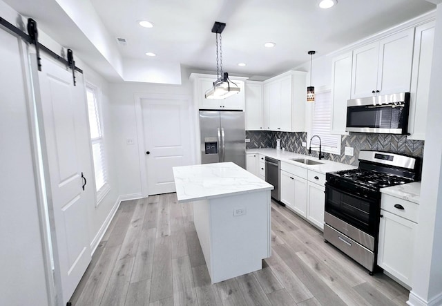 kitchen with pendant lighting, sink, a barn door, a kitchen island, and stainless steel appliances