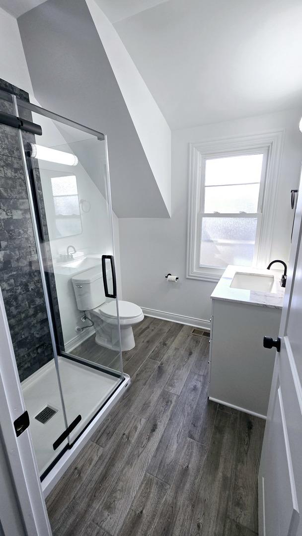 bathroom featuring vanity, lofted ceiling, hardwood / wood-style flooring, toilet, and a shower with shower door