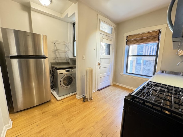 kitchen featuring radiator heating unit, stainless steel refrigerator, washer / clothes dryer, sink, and black gas range