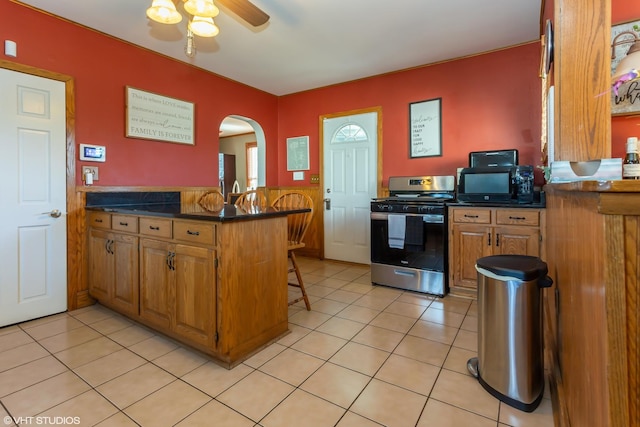 kitchen with ceiling fan, kitchen peninsula, a kitchen bar, light tile patterned floors, and stainless steel range with gas stovetop