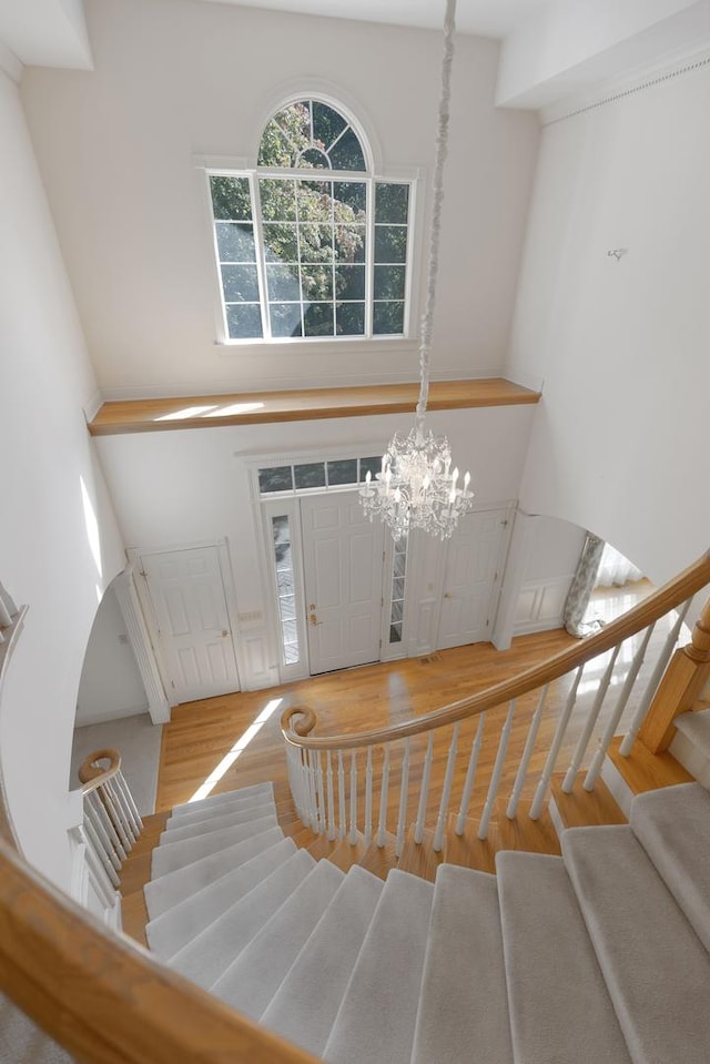 staircase with hardwood / wood-style floors, an inviting chandelier, and a high ceiling