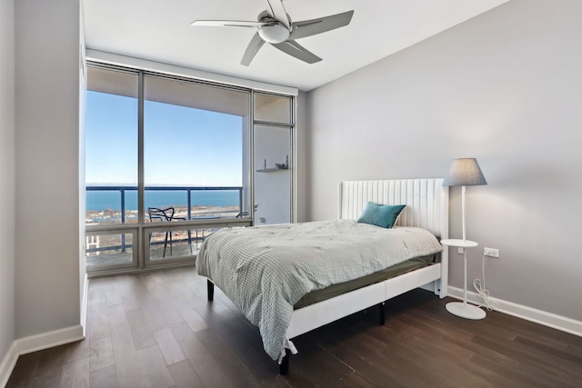 bedroom featuring ceiling fan, a water view, dark hardwood / wood-style floors, and a wall of windows