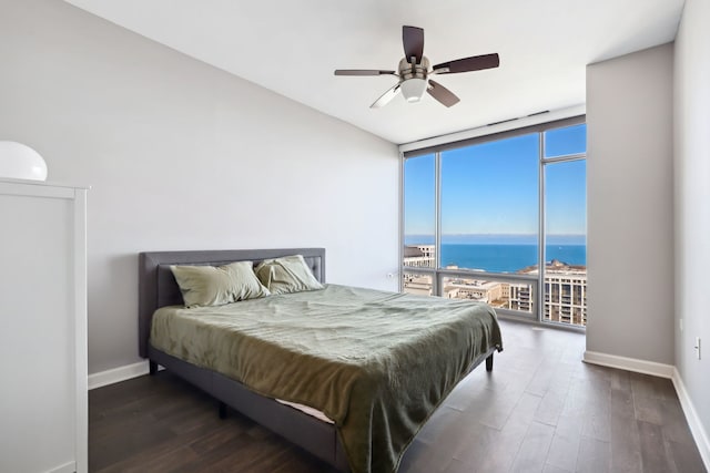 bedroom with ceiling fan, dark hardwood / wood-style flooring, a water view, and a wall of windows