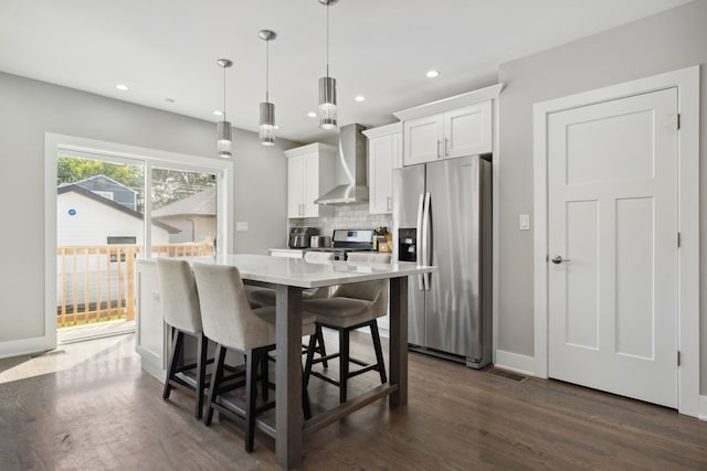 kitchen with wall chimney range hood, pendant lighting, a kitchen bar, white cabinets, and appliances with stainless steel finishes