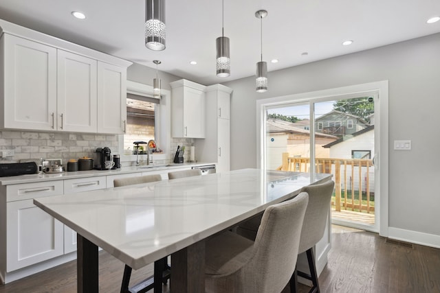 kitchen featuring pendant lighting, dark wood-type flooring, decorative backsplash, light stone countertops, and white cabinetry