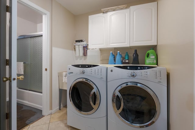 clothes washing area featuring cabinets, washing machine and dryer, and light tile patterned floors