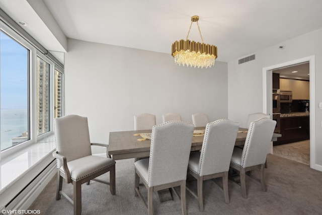 carpeted dining area with a water view, a baseboard radiator, and a chandelier